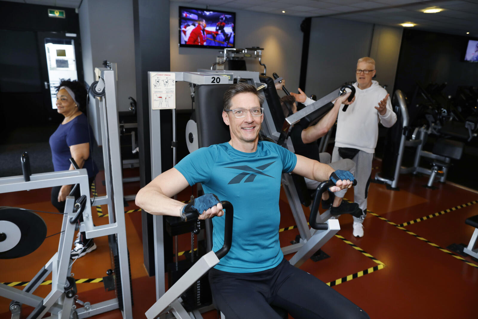 Bij Fitness America van Dick Huisman (witte sweater), ‘een Rotterdamse ondernemer die naast alle COVID-ellende ook met ziekte kreeg te kampen. Hij knokt zich er elke dag weer vrolijk doorheen, en is ook nog eens politiek geïnteresseerd.’