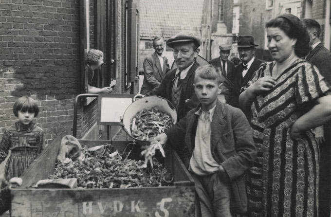 Het is zo te zien een hele gebeurtenis. De Utrechtse schillenboer leegt een emmer in zijn bakfiets onder toeziend oog van de buurtbewoners