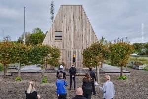 mensen staan voor een verkeerslicht dat op oranje staat, daarachter een nieuw huis. Symbolisch voor de bouw die stilstaat
